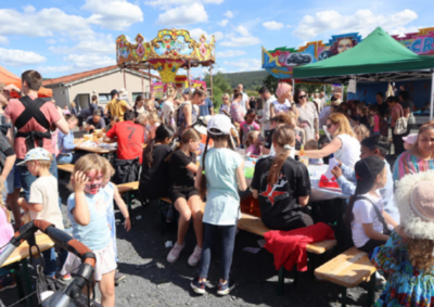 Auf dem Bild sieht man ein Kinderkarusell im Hintergrund, davor viele Menschen die auf einem Rummel oder Fest sind.