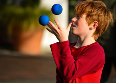Das Bild zeigt einen Jungen der blaue Bälle jongliert
