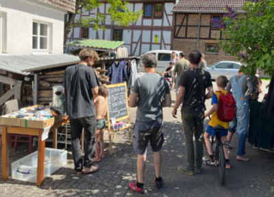 Das Bild zeigt verschiedene Personen - klein und groß - von hinten an Verschenkeständen stehen